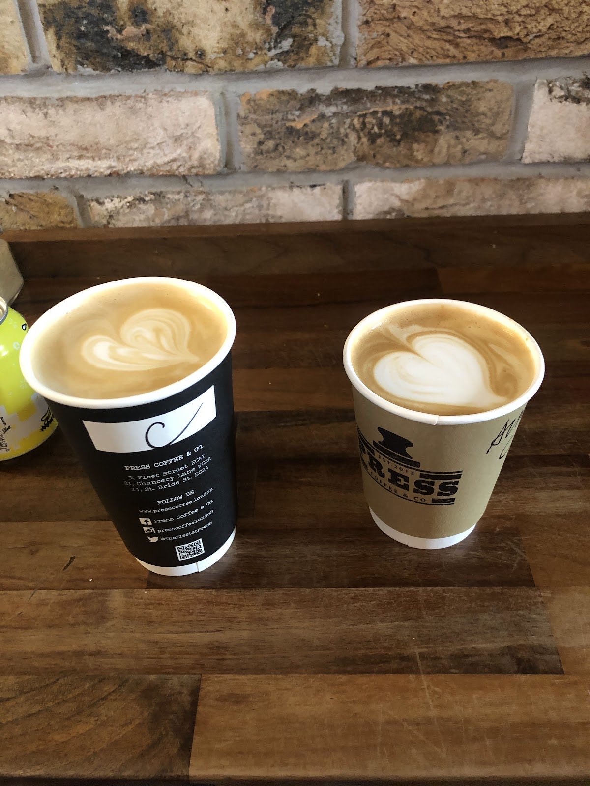 Two takeaway coffee cups side by side on a wooden ledge